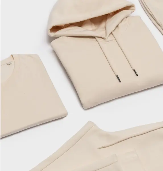 Ensemble de vêtements beiges pliés, comprenant un sweat à capuche, un t-shirt et un pantalon.